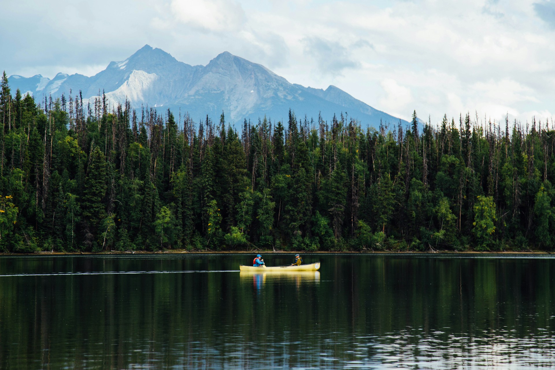 Two people in a yellow boat sailing near pine trees during daytime at Bowron Lake, B.C.