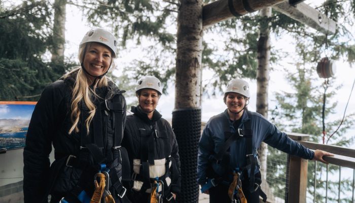 Three women wearing helmet on a forest platform are smiling.