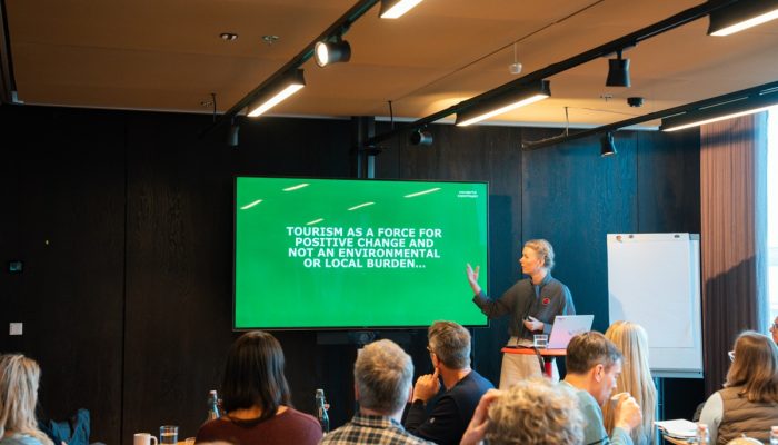 "Tourism as a force for positive change and not an environmental burden..." appears on a slide, where a woman is pointing.