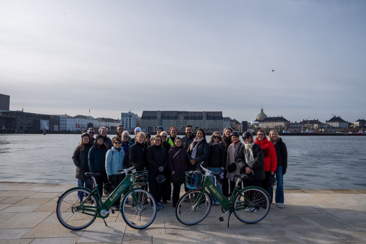 A group of about 20 people takes a photo together with bicycles at the Copenhagen waterfront.