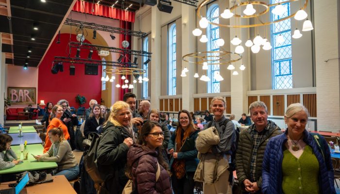 A group stands in a bright and spacious common area. A "bar" sign is in the background.