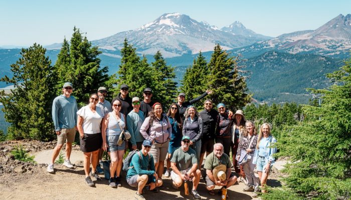 About 20 people pose and smile to the camera on a mountaintop.