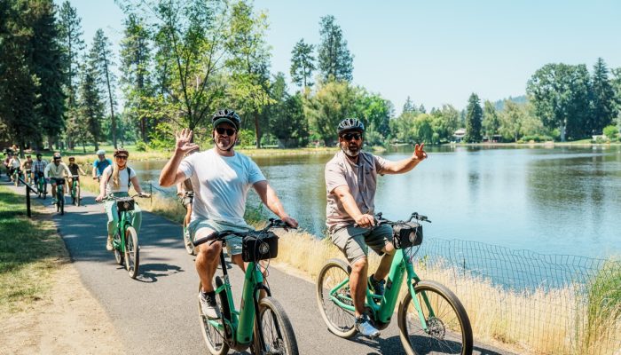 Two people riding bikes wave to the camera.